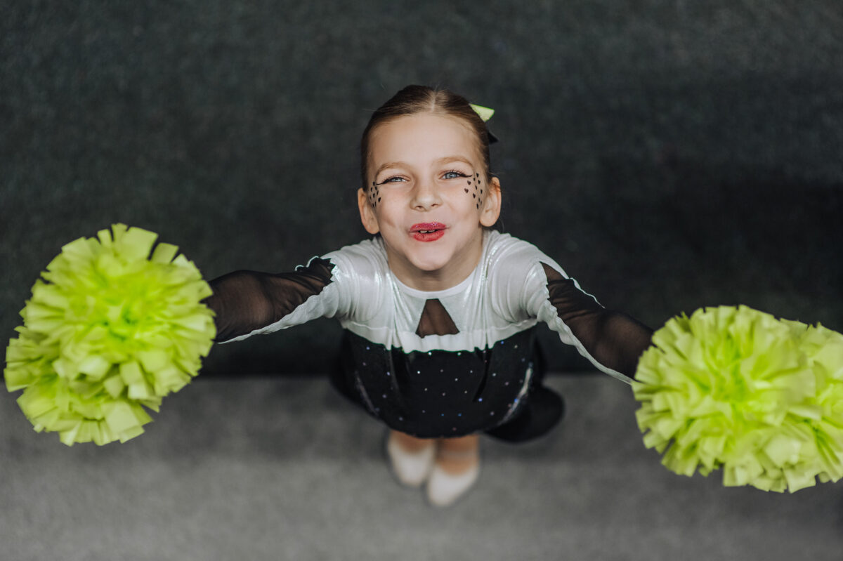 Smiling happy girl athlete cheerleader in a suit with pompoms